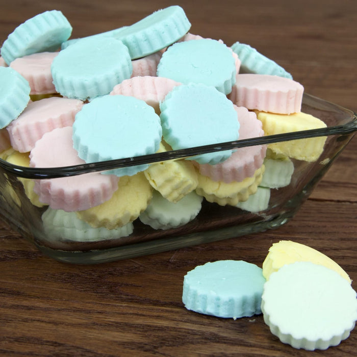 A glass bowl filled with pastel-colored butter mints sits on a wooden surface.
