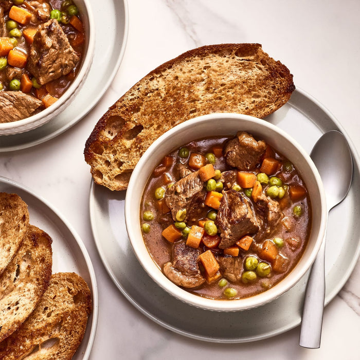 A bowl of beef stew with carrots and peas served with toasted bread.