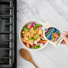A hand pours Starkist Tuna Creations into a bowl of fresh vegetables.