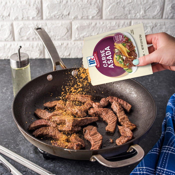 A hand pours McCormick Carne Asada seasoning onto strips of beef in a frying pan.