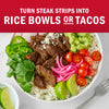A steak strip rice bowl with toppings like guacamole, tomatoes, and pickled onions is shown with the text Turn steak strips into rice bowls or tacos.