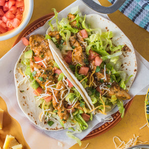 A delicious taco filled with seasoned chicken, fresh lettuce, diced tomatoes, avocado, and cheese, presented on a decorative plate.