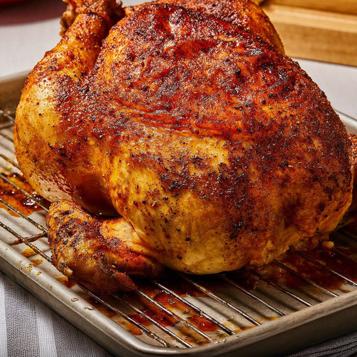 A whole roasted bird rests on a wire rack after being seasoned with Mccormick Perfect Pinch Rotisserie Chicken Seasoning Powder 5 Oz to achieve a golden brown and crispy skin.
