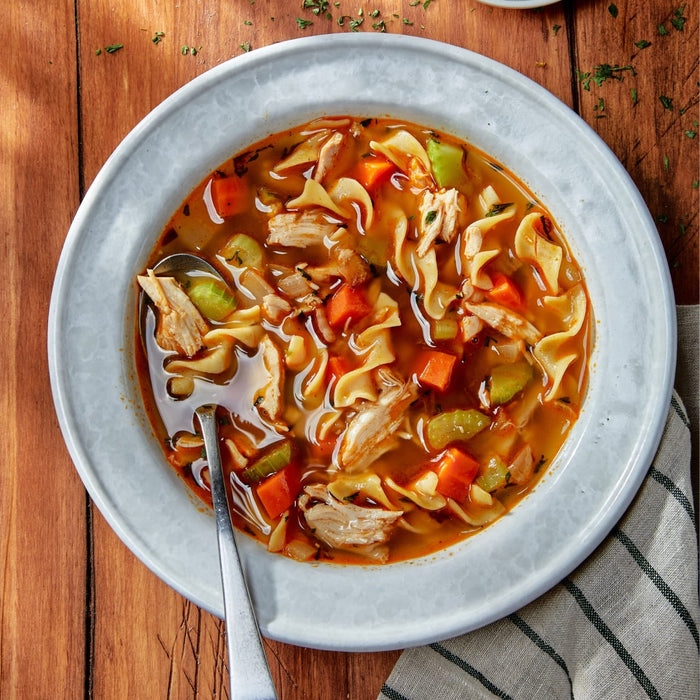 A warm bowl of chicken noodle soup featuring tender chicken pieces seasoned with Mccormick Perfect Pinch Rotisserie Chicken Seasoning Powder 5 Oz alongside wide egg noodles and fresh vegetables.