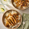 A top-down view of two bowls featuring sliced chicken breast seasoned with Mccormick Perfect Pinch Cajun Seasoning Ground 5 Oz served over a bed of white rice with a savory sauce.