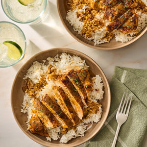 A top-down view of two bowls featuring sliced chicken breast seasoned with Mccormick Perfect Pinch Cajun Seasoning Ground 5 Oz served over a bed of white rice with a savory sauce.