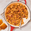 A large red skillet filled with a hearty jambalaya made with rice, chicken, and sausage seasoned with Mccormick Perfect Pinch Cajun Seasoning Ground 5 Oz alongside pieces of golden cornbread.