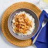 A top-down view of a grey bowl filled with white rice and shrimp seasoned with Mccormick Perfect Pinch Cajun Seasoning Ground 5 Oz placed on a woven charger next to a blue napkin and a glass of water.
