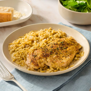 A seasoned chicken breast rests on a bed of creamy orzo, showcasing the vibrant flavors of Mccormick Signature Seasoning Lemon Pepper Oz alongside a fresh green salad and parmesan cheese.