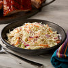 A bowl of creamy coleslaw is seasoned with Mccormick Signature Seasoning Lemon Pepper Oz and served alongside grilled barbecue ribs.