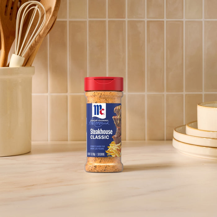A bottle of Mccormick Perfect Pinch Steak Seasoning Ground 7 Oz stands on a marble countertop in a bright kitchen setting.