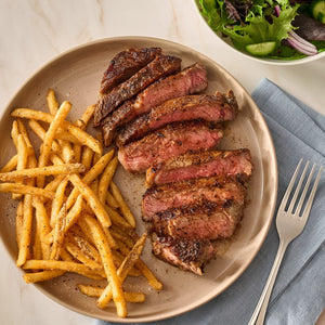 A plate of sliced medium-rare steak and seasoned french fries prepared with Mccormick Perfect Pinch Steak Seasoning Ground 7 Oz alongside a fresh green salad.