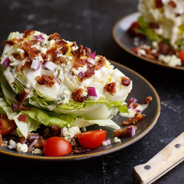 A crisp wedge salad is beautifully presented on a dark plate and seasoned with Mccormick Perfect Pinch Steak Seasoning Ground 7 Oz along with bacon bits, blue cheese crumbles, red onions, and cherry tomatoes.