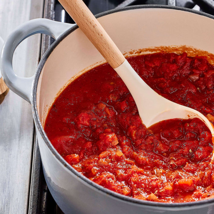 A pot of simmering tomato sauce is being stirred with a wooden spoon.