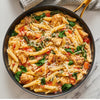 A skillet of penne pasta with chicken, spinach, and tomatoes, topped with grated cheese.