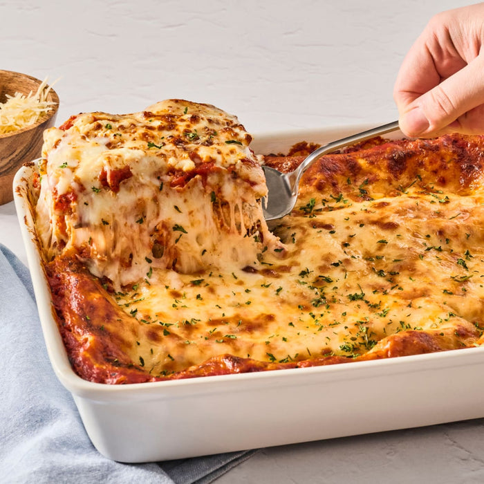 A skillet of penne pasta with chicken, spinach, and tomatoes, topped with grated cheese.