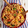 A vibrant pasta salad featuring rotini, broccoli, carrots, and tomatoes is tossed with Mccormick Signature Seasoning Salad Supreme Oz in a red bowl.