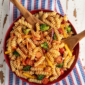 A vibrant pasta salad featuring rotini, broccoli, carrots, and tomatoes is tossed with Mccormick Signature Seasoning Salad Supreme Oz in a red bowl.