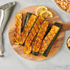 Grilled zucchini spears are seasoned with Mccormick Signature Seasoning Salad Supreme Oz and served on a wooden board with charred lemon slices.