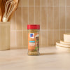 A bottle of Mccormick Onion And Herb Seasoning Crystal 4.16 Oz stands on a marble countertop in a bright kitchen setting with wooden utensils and plates in the background.