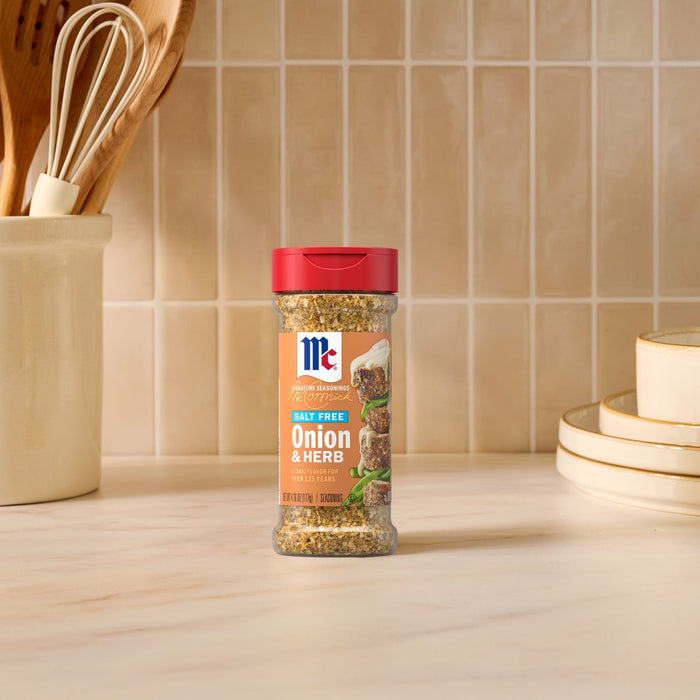 A bottle of Mccormick Onion And Herb Seasoning Crystal 4.16 Oz stands on a marble countertop in a bright kitchen setting with wooden utensils and plates in the background.