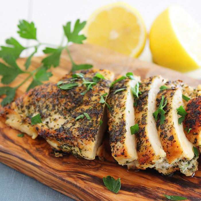 A sliced chicken breast rests on a wooden board seasoned with Mccormick Onion And Herb Seasoning Crystal 4.16 Oz and garnished with fresh parsley and lemon.