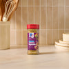 A bottle of Mccormick Vegetable Seasoning Assorted Form 4.16 Oz stands on a marble countertop in a kitchen setting with cooking utensils and plates in the background.
