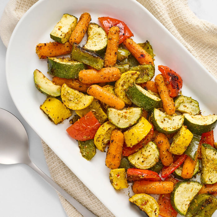 A white serving platter holds a colorful medley of roasted zucchini, yellow squash, carrots, and bell peppers seasoned with Mccormick Vegetable Seasoning Assorted Form 4.16 Oz.