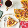 A slice of savory quiche topped with bacon and herbs sits on a plate next to a cup of coffee and a bowl of berries, seasoned with Mccormick Vegetable Seasoning Assorted Form 4.16 Oz.
