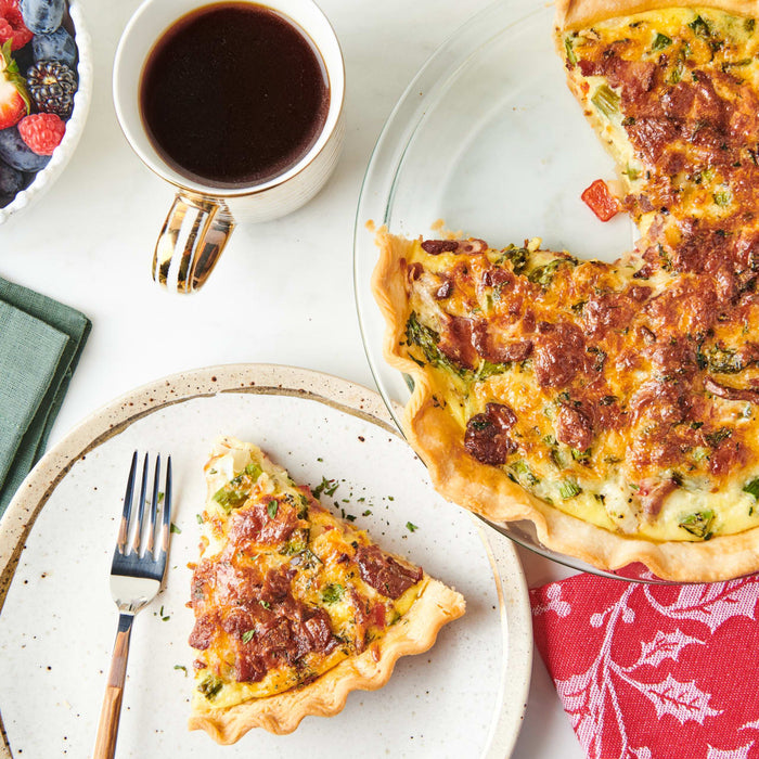 A slice of savory quiche topped with bacon and herbs sits on a plate next to a cup of coffee and a bowl of berries, seasoned with Mccormick Vegetable Seasoning Assorted Form 4.16 Oz.