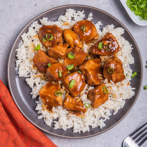 A plate of teriyaki chicken served over white rice, garnished with green onions.