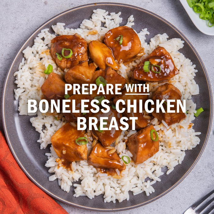 A plate of rice topped with boneless chicken breast pieces and sauce.