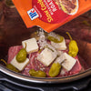 A McCormick Slow Cookers Mississippi Roast seasoning packet is being poured over a roast with butter and peppers in a slow cooker.