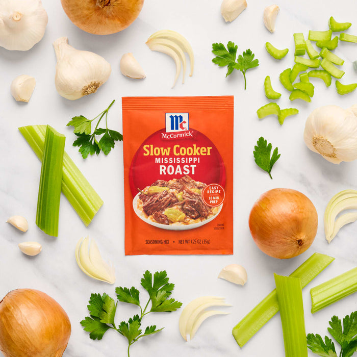 A packet of McCormick Slow Cookers Pot Roast seasoning mix is surrounded by fresh ingredients like onions, garlic, celery, and parsley.