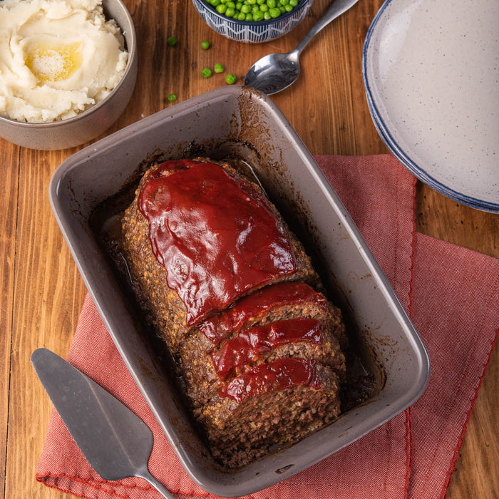 ['A meatloaf with a red glaze is in a baking dish on a red napkin.']