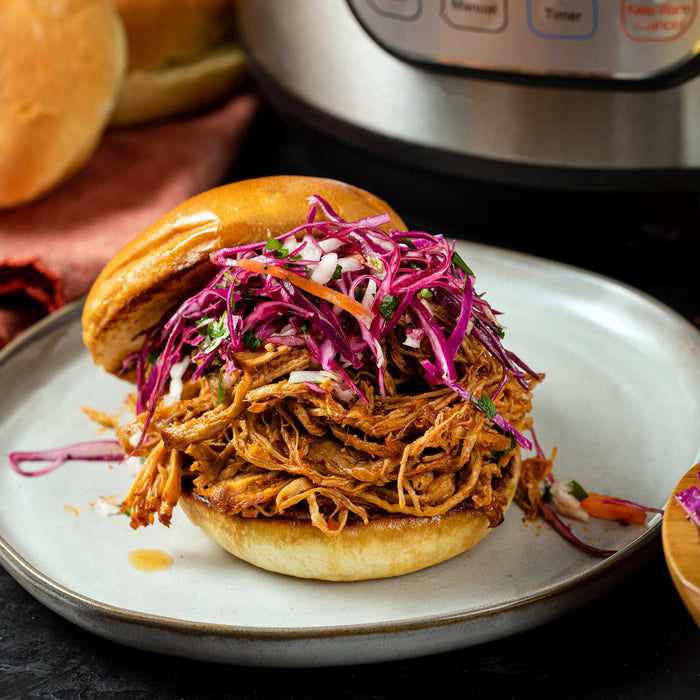A pulled pork sandwich with red cabbage slaw on a white plate.