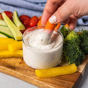 ['A hand dips a baby carrot into a bowl of ranch dressing.']
