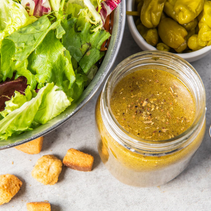 ['A bowl of salad with croutons and a jar of salad dressing.']