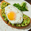 ['A close-up of avocado toast topped with a fried egg and sprinkled with red pepper flakes.']