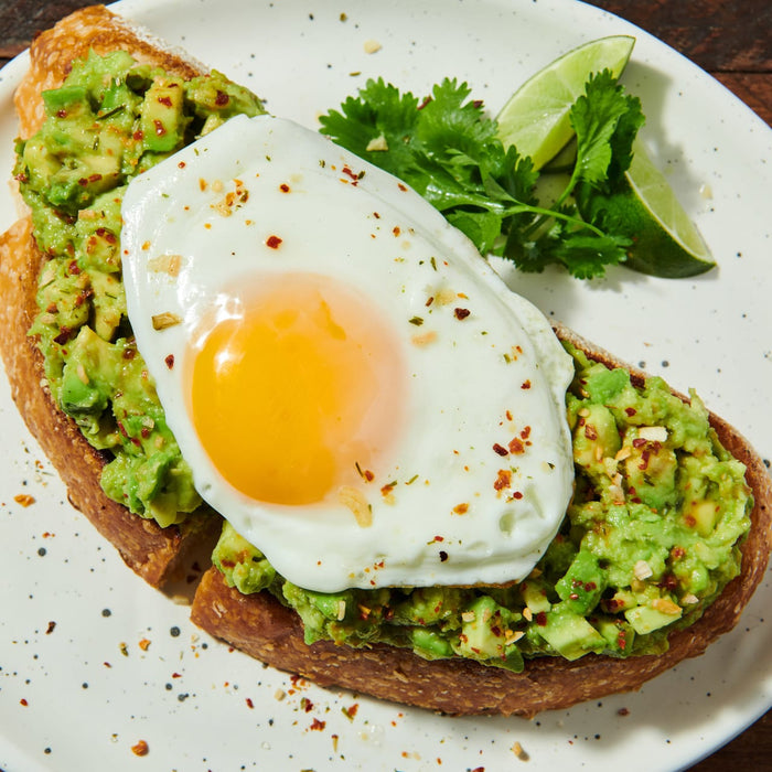 ['A close-up of avocado toast topped with a fried egg and sprinkled with red pepper flakes.']