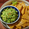 ['A bowl of guacamole with tortilla chips and a lime wedge.']