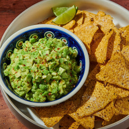 ['A bowl of guacamole with tortilla chips and a lime wedge.']