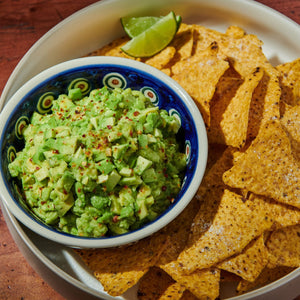 ['A bowl of guacamole with tortilla chips and a lime wedge.']