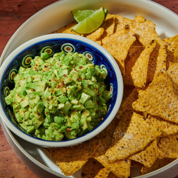 ['A bowl of guacamole with tortilla chips and a lime wedge.']