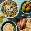 ['A plate of Middle Eastern food with tabbouleh, hummus, olives, pita bread, and a lemon wedge.']