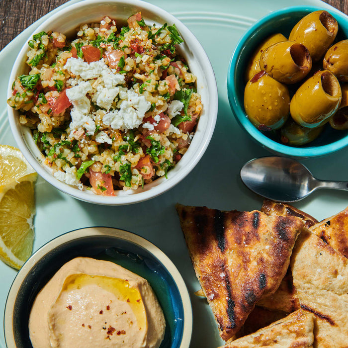 ['A plate of Middle Eastern food with tabbouleh, hummus, olives, pita bread, and a lemon wedge.']