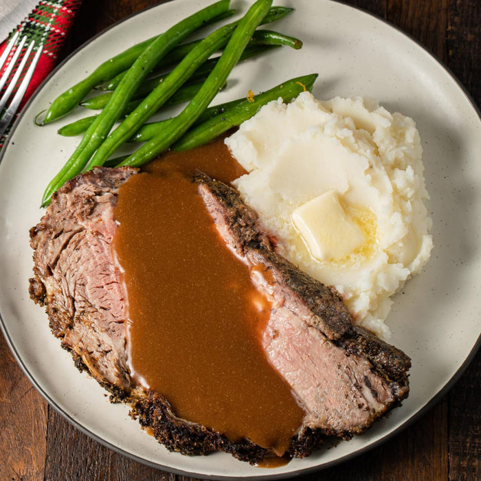 ['A plate of prime rib with mashed potatoes, green beans, and gravy.']