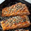 ['Two pieces of salmon are grilled and covered in sesame seeds.']