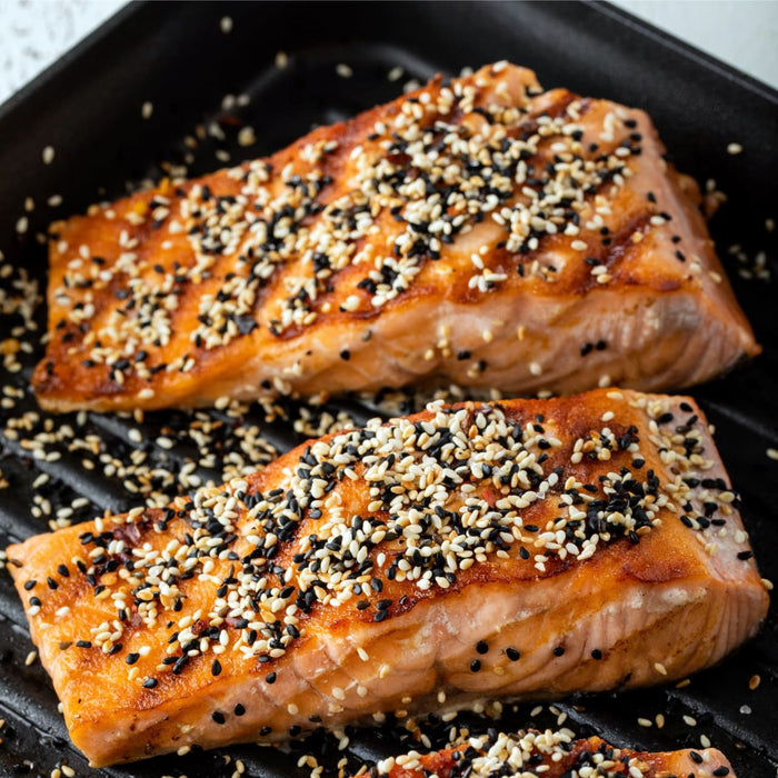 ['Two pieces of salmon are grilled and covered in sesame seeds.']
