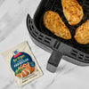 McCormick Air Fryer Parmesan seasoning mix is shown next to an air fryer with cooked chicken breasts inside.